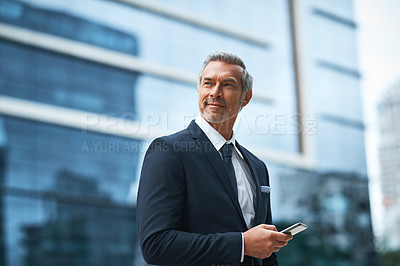 Buy stock photo Shot of a handsome mature businessman in corporate attire using a cellphone outside outside during the day