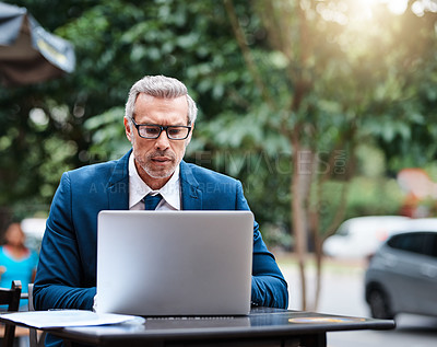 Buy stock photo Shot of a handsome mature business in corporate attire using a laptop outside during the day