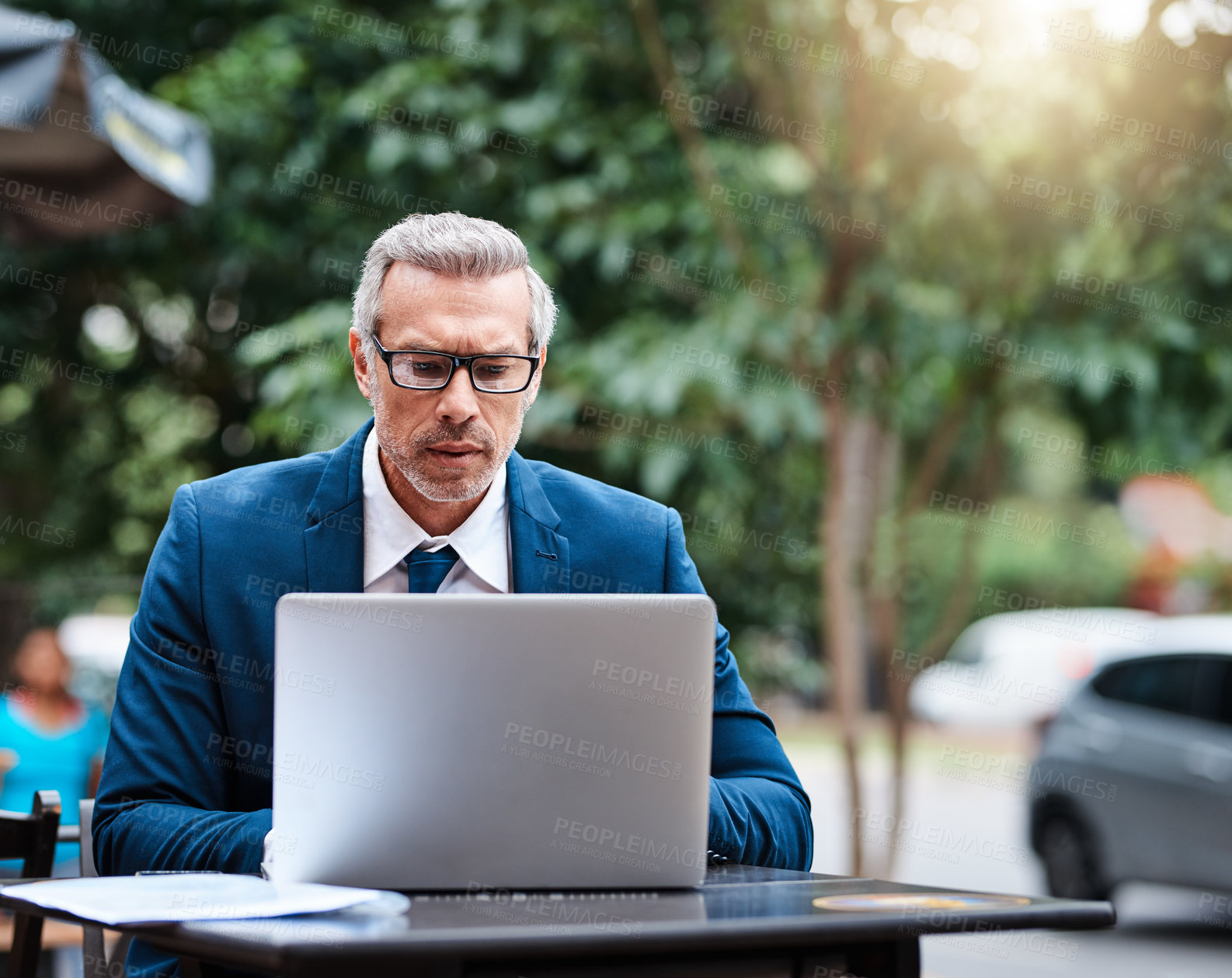Buy stock photo Shot of a handsome mature business in corporate attire using a laptop outside during the day