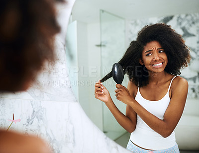 Buy stock photo Shot of an attractive young woman struggling to comb her hair at home
