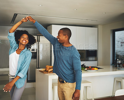 Buy stock photo Shot of a cheerful young couple dancing together in the kitchen at home during the day