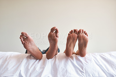Buy stock photo Cropped shot of an unrecognizable couple’s bare feet on the edge of the bed at home