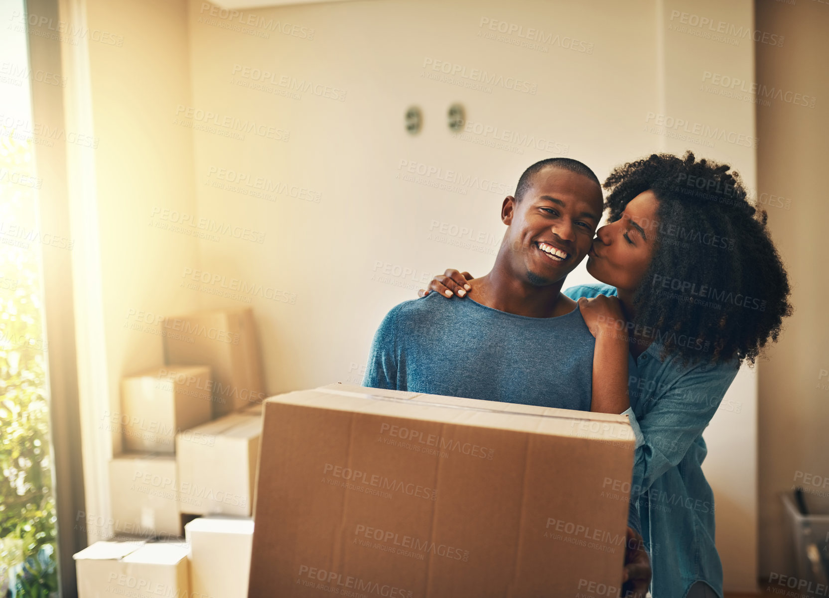 Buy stock photo New house, boxes and couple with kiss for moving, real estate or property investment in living room. Lens flare, black man and young woman with cardboard for love, mortgage or relocation in home