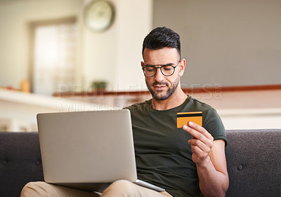Buy stock photo Shot of a handsome young man using a laptop and credit card at home