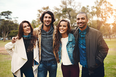 Buy stock photo Portrait of a group of cheerful young friends huddled together while standing in a park outside during the day
