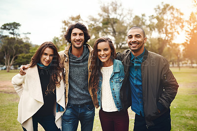 Buy stock photo Portrait of a group of cheerful young friends huddled together while standing in a park outside during the day