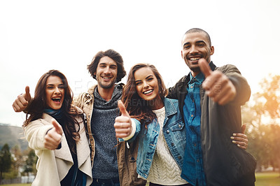 Buy stock photo Portrait of a group of cheerful young friends huddled together while showing thumbs up outside during the day