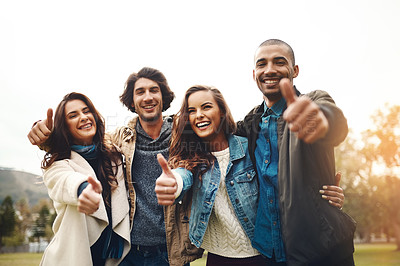 Buy stock photo Portrait of a group of cheerful young friends huddled together while showing thumbs up outside during the day