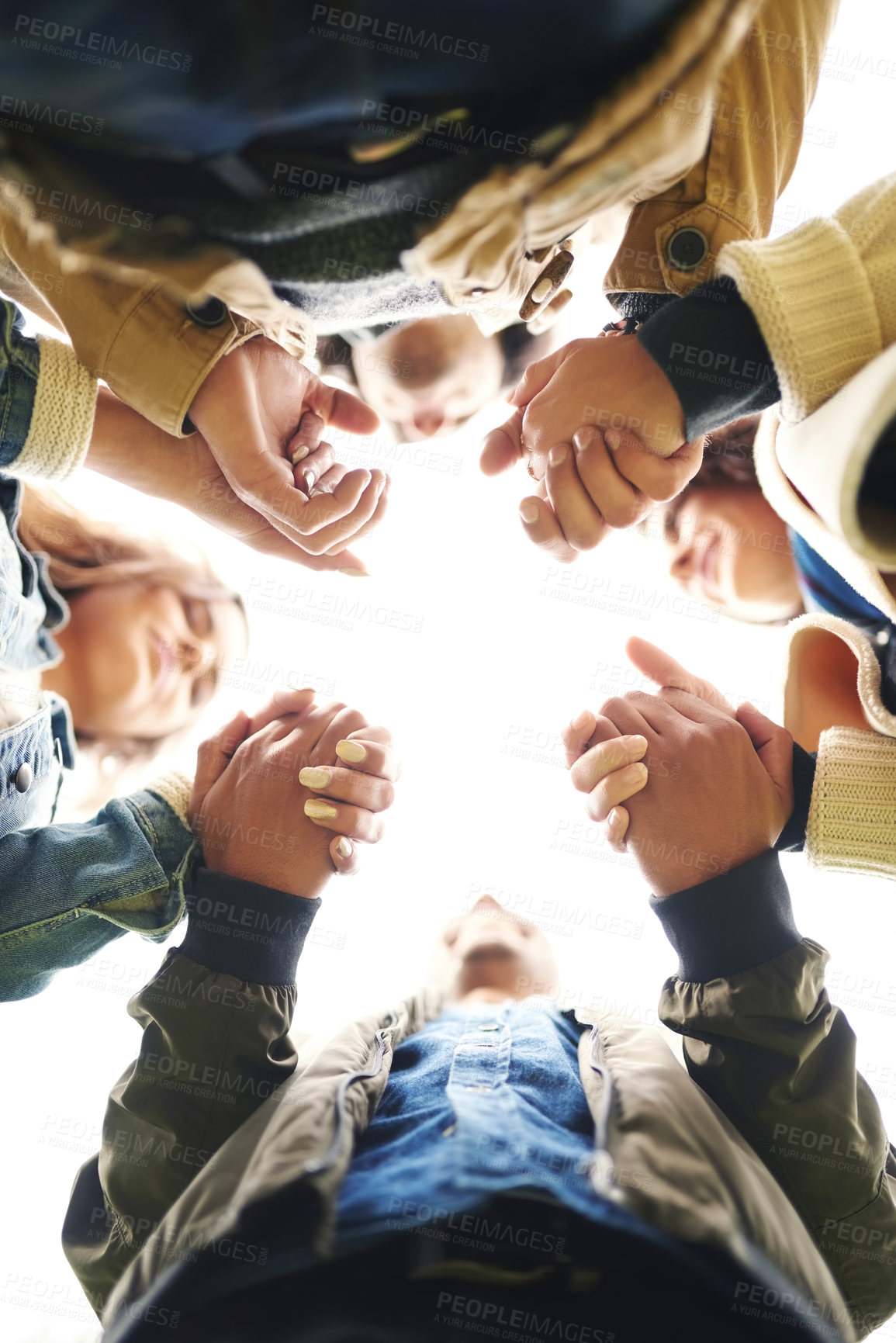 Buy stock photo Low angle portrait of a group of young friends huddled together while holding hands outside during the day