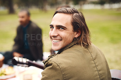 Buy stock photo Portrait of a cheerful young man seated with his friends at a picnic outside during the day