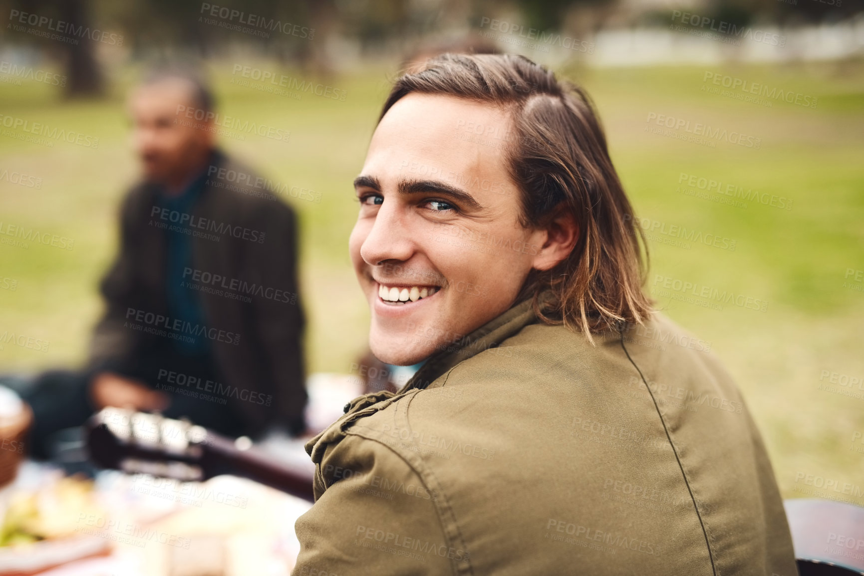 Buy stock photo Portrait of a cheerful young man seated with his friends at a picnic outside during the day