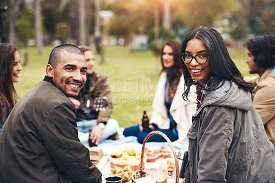 Buy stock photo Portrait of two cheerful young people seated at a picnic with friends outside during the day