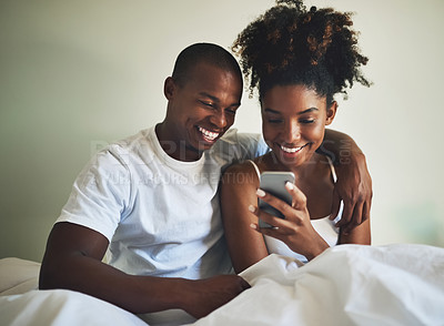 Buy stock photo Shot of a happy young couple using a mobile phone together in bed at home