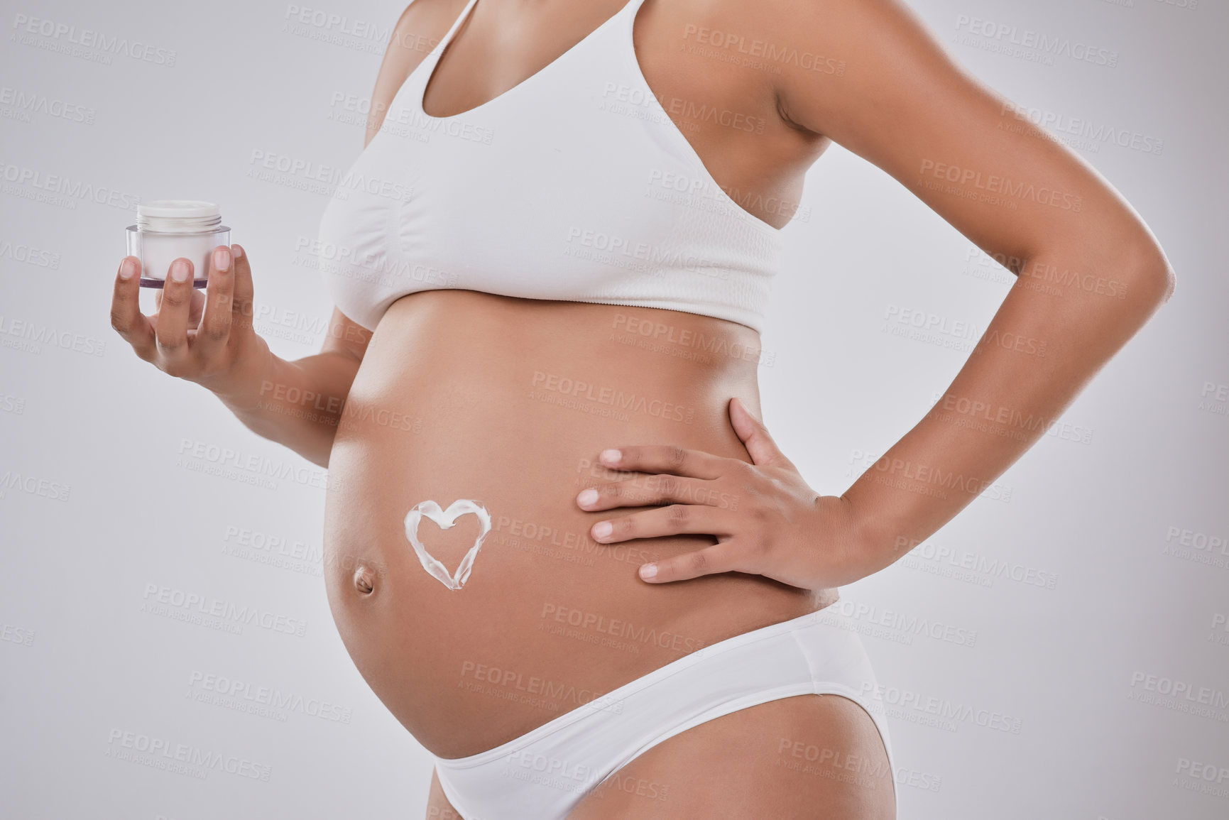 Buy stock photo Hands, pregnant woman and skincare cream in studio, heart sign or belly with cosmetics by white background. Body, mother and container with serum, creme or product to clear stretch marks on stomach