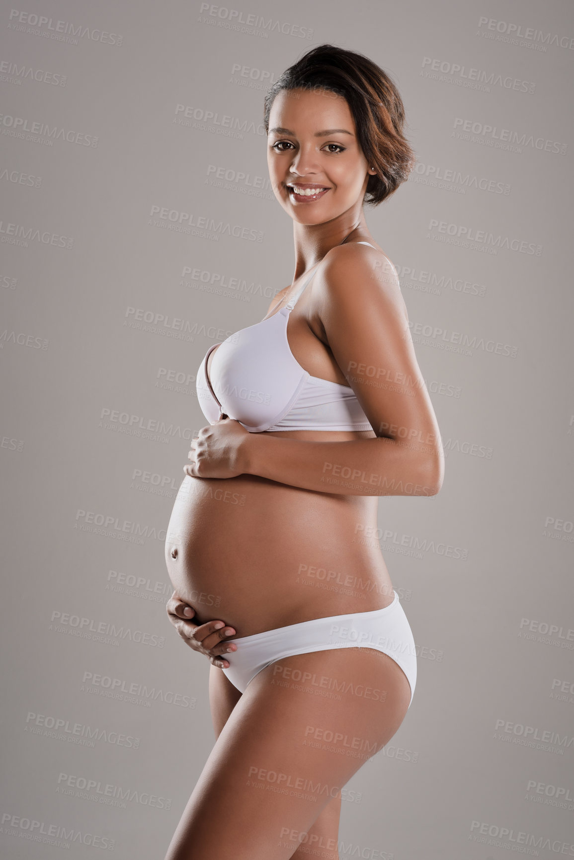 Buy stock photo Studio portrait of a beautiful young pregnant woman posing in underwear against a gray background