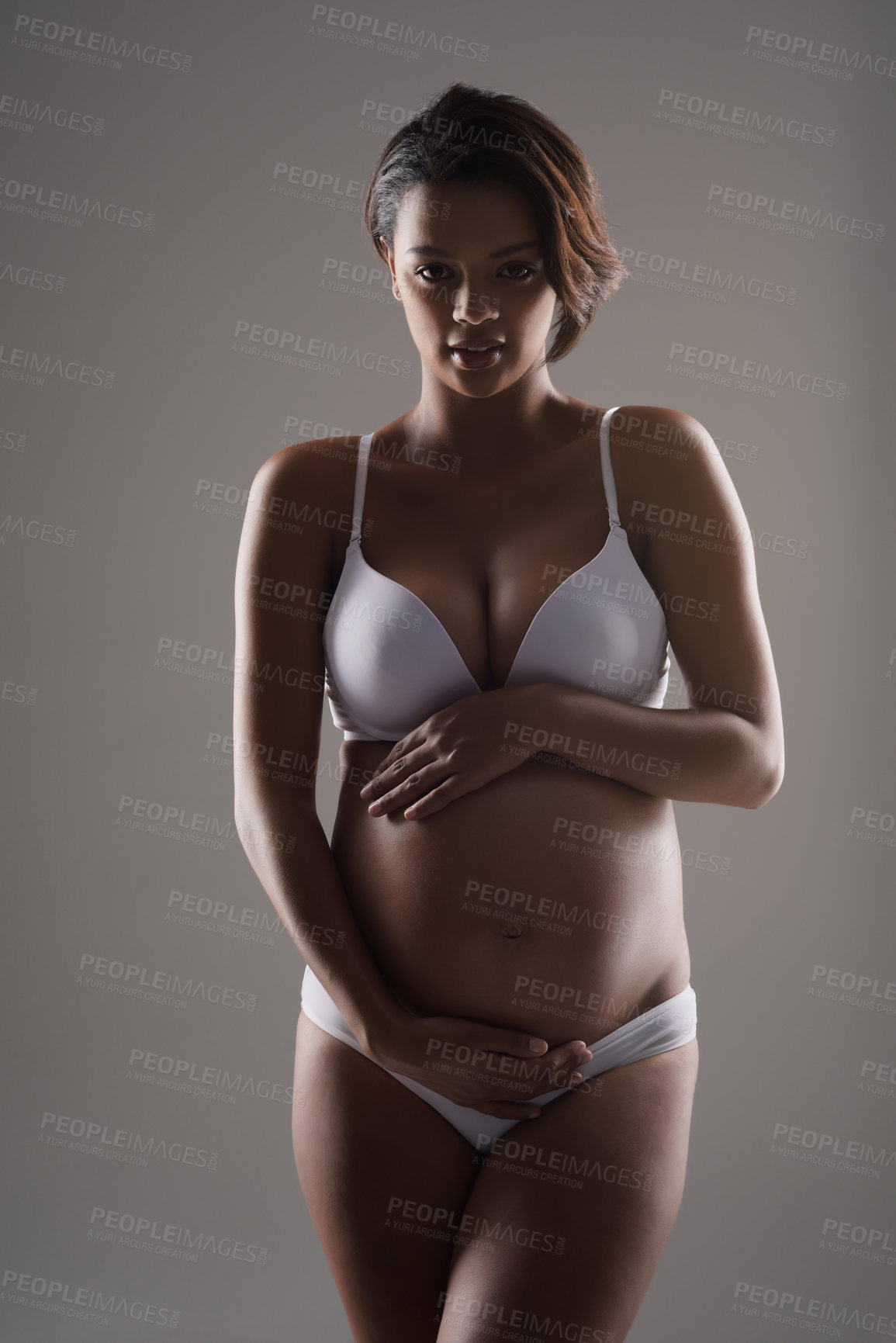 Buy stock photo Studio portrait of a beautiful young pregnant woman posing in underwear against a gray background