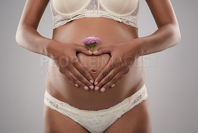 Buy stock photo Studio shot of an unrecognizable pregnant woman making a heart shape with her hands on top of her belly against a gray background