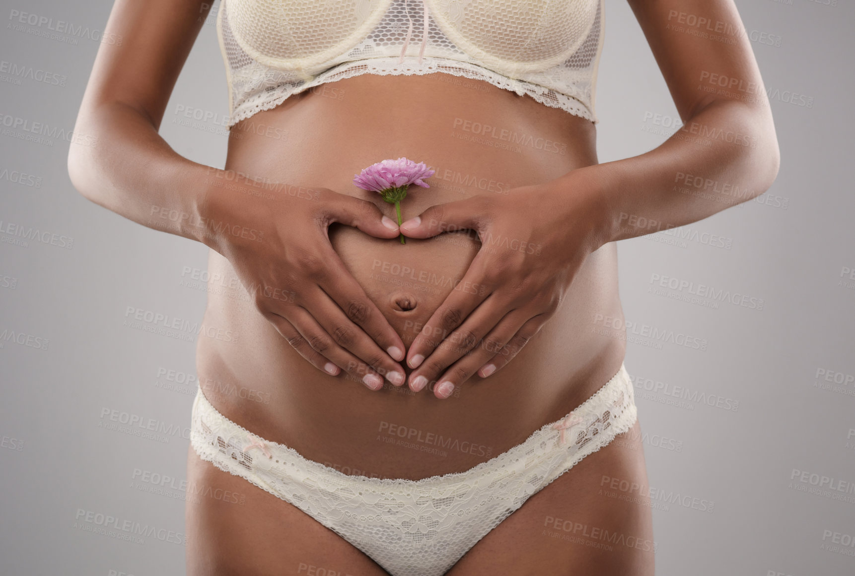 Buy stock photo Studio shot of an unrecognizable pregnant woman making a heart shape with her hands on top of her belly against a gray background