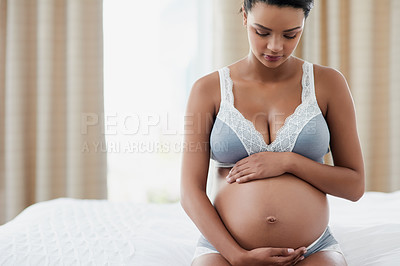 Buy stock photo Shot of a pregnant young woman sitting on her bed at home