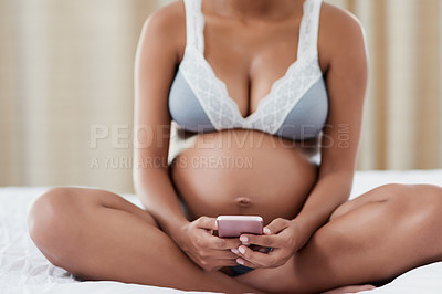 Buy stock photo Shot of a pregnant young woman using a cellphone while sitting on her bed at home