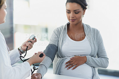 Buy stock photo Shot of a confident female doctor checking the blood pressure of a pregnant patient at a hospital during the day