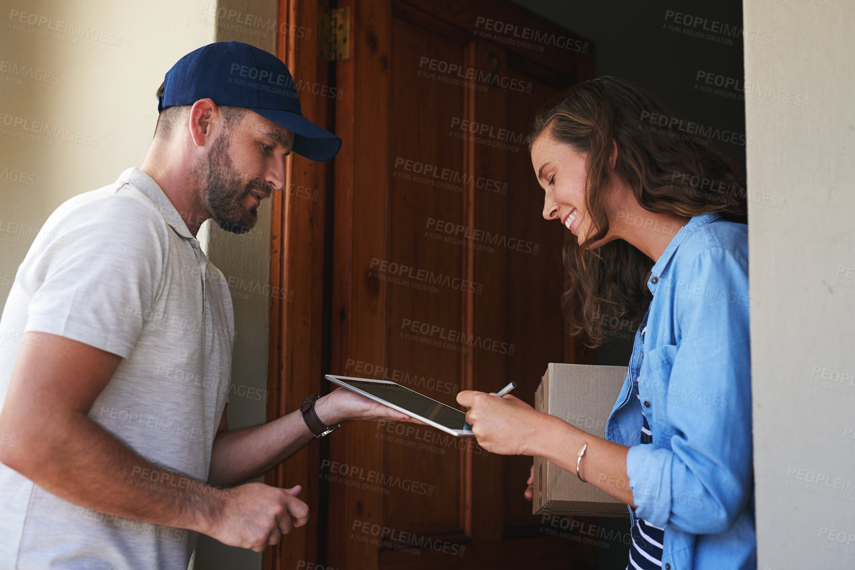 Buy stock photo Shot of a young woman using a digital tablet to sign for her delivery from the courier