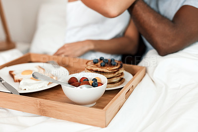 Buy stock photo Shot of an unrecognizable couple enjoying breakfast in bed together at home during the day