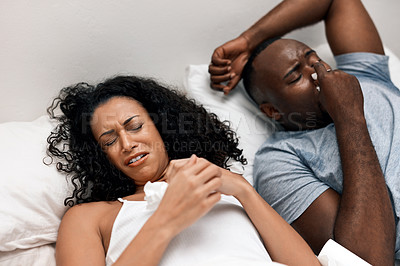 Buy stock photo Shot of a irritated looking young woman lying in bed with her husband and trying to get some sleep but can't due to his snoring