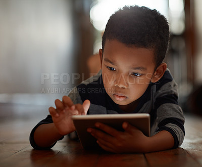 Buy stock photo Little boy, browsing and on digital tablet or playing games or streaming video on the internet and lying on the floor at home on bokeh. Technology, device and male child downloading app or reading 