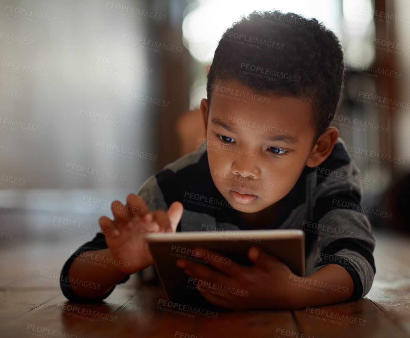 Buy stock photo Little boy, browsing and on digital tablet or playing games or streaming video on the internet and lying on the floor at home on bokeh. Technology, device and male child downloading app or reading 