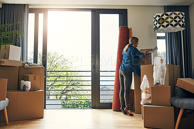 Buy stock photo Rearview shot of a focused middle aged woman packing out a box at her new home inside during the day