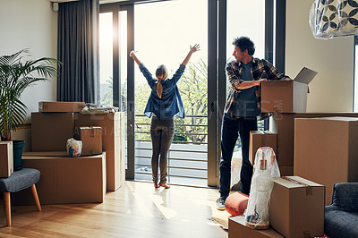 Buy stock photo Shot of a cheerful middle aged woman stretching her arms out on her balcony while her husband looks at her and packs out boxes on moving day