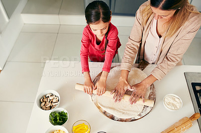 Buy stock photo High angle shot of a middle aged mother and her daughter preparing a pizza to go into the oven in the kitchen at home