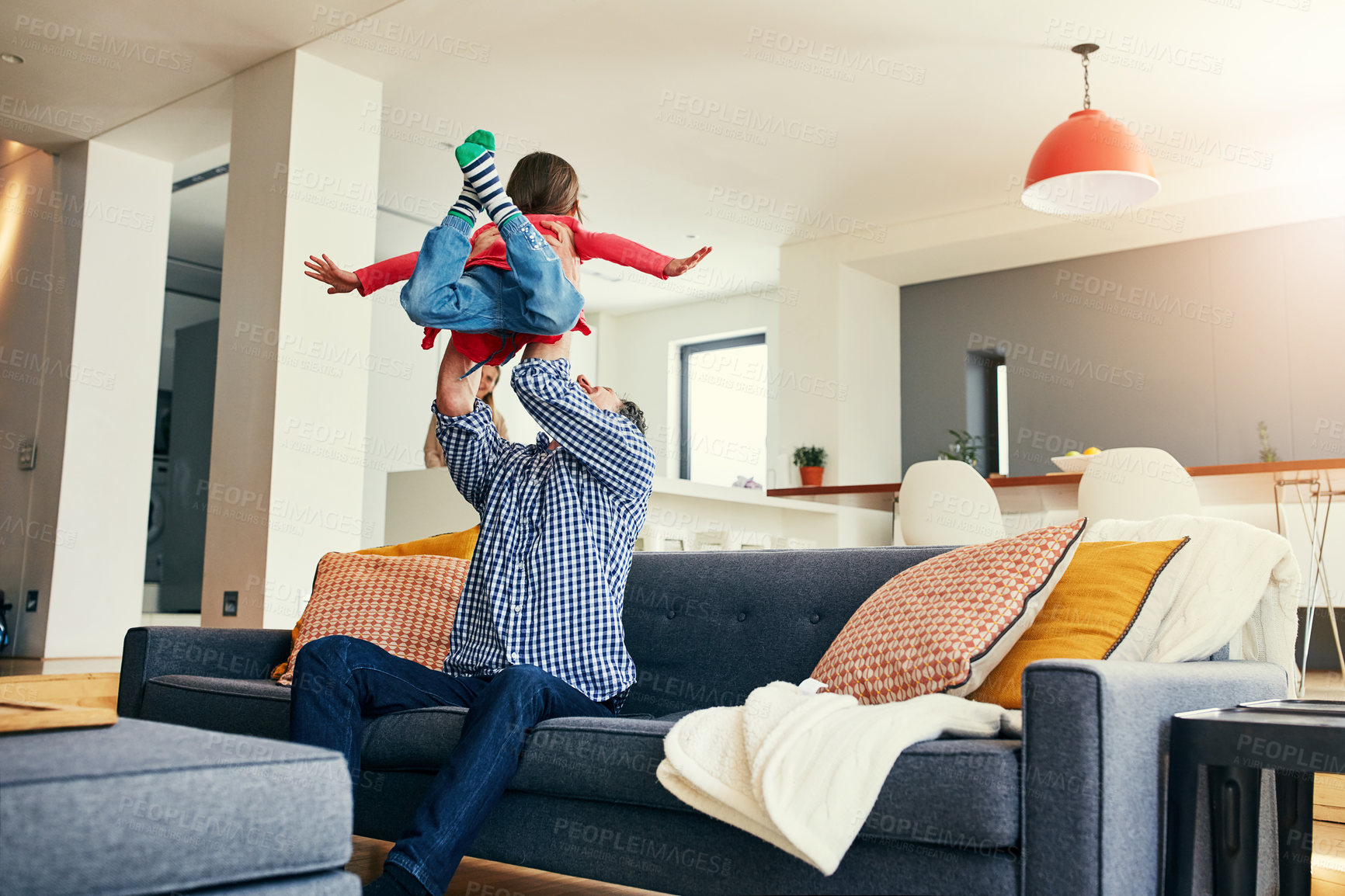 Buy stock photo Shot of a cheerful middle aged father holding his young daughter in the air while playing and being seated on the couch at home during the day