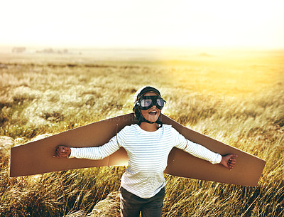 Buy stock photo Shot of a young boy pretending to fly with a pair of cardboard wings in an open field