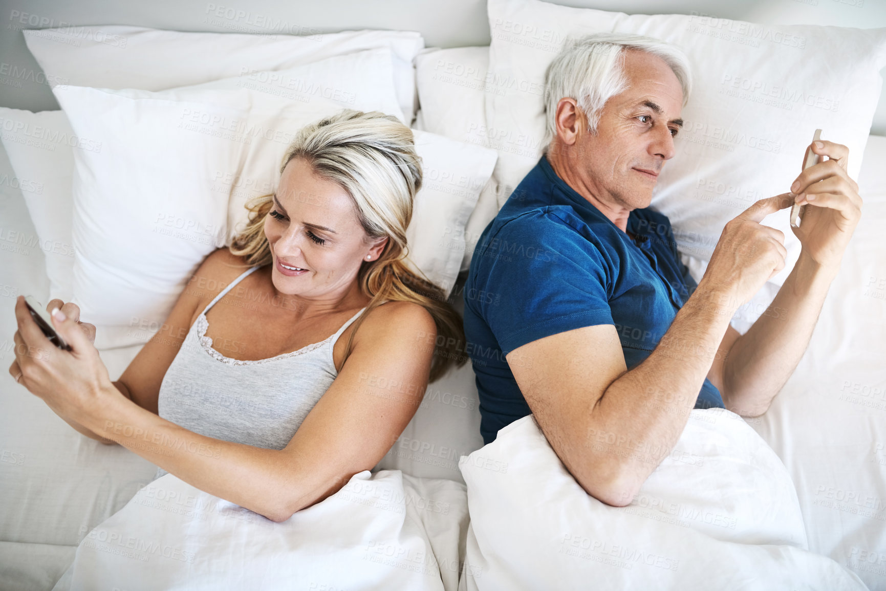 Buy stock photo Shot of a mature couple using their cellphones in bed at home