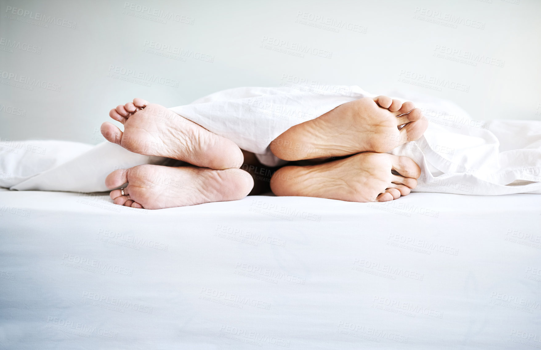 Buy stock photo Shot of a couple's bare feet sticking out underneath the bedsheets at home