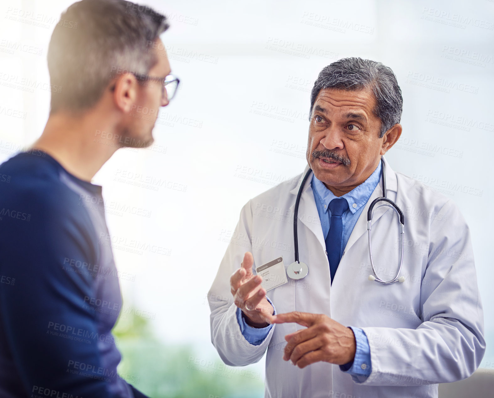 Buy stock photo Shot of a confident mature male doctor consulting a patient while standing inside a hospital during the day