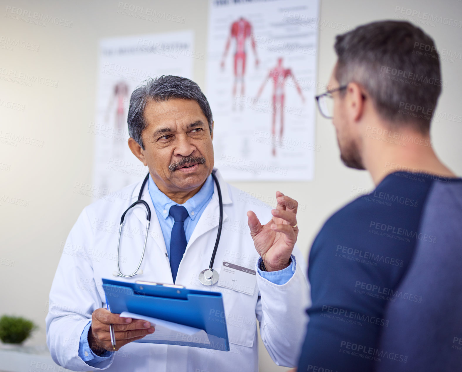 Buy stock photo Shot of a confident mature male doctor consulting a patient while standing inside a hospital during the day