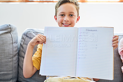 Buy stock photo Cropped shot of a little boy holding up a notebook with his homework in it on the sofa at home