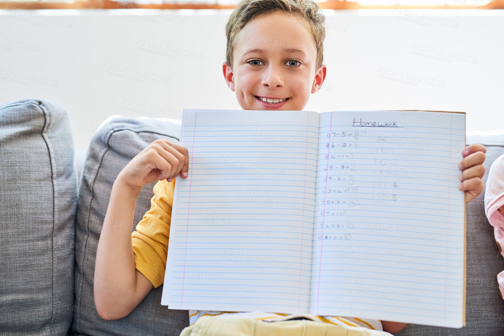 Buy stock photo Cropped shot of a little boy holding up a notebook with his homework in it on the sofa at home