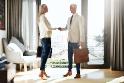 Buy stock photo Shot of two confident businesspeople shaking hands in agreement inside a house during the day