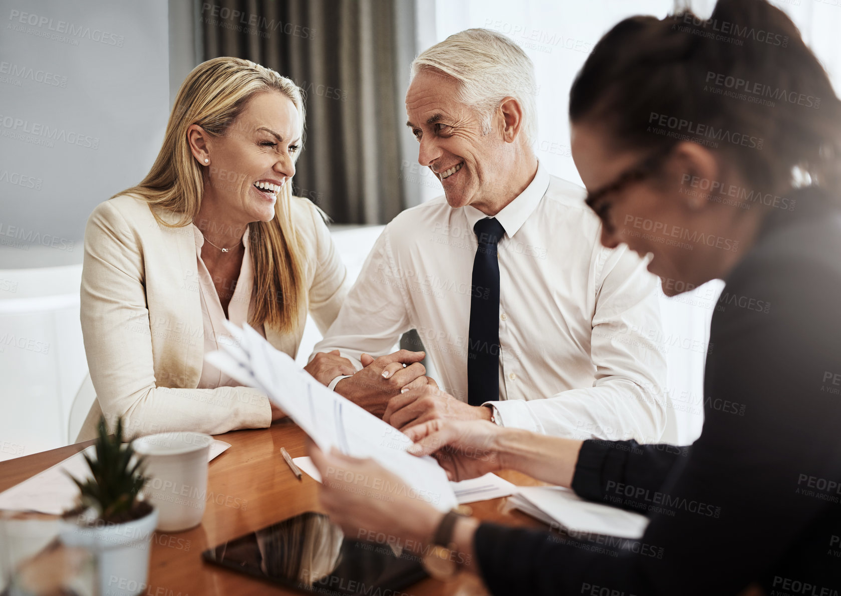 Buy stock photo Shot of a cheerful mature couple negotiating with a architect over house plans around a table inside of a building during the day
