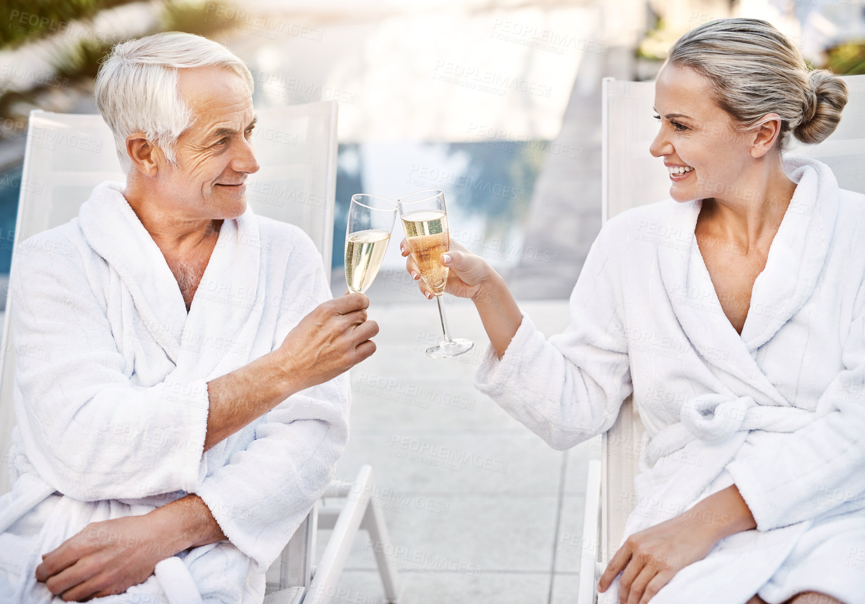 Buy stock photo Shot of a cheerful middle aged couple having a celebratory toast with champagne outside during the day
