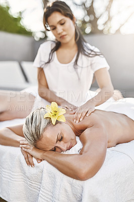 Buy stock photo Shot of a relaxed middle aged woman lying on her stomach while receiving a massage at a spa outside during the day