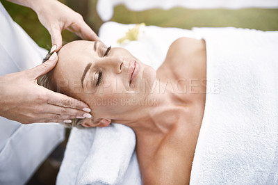 Buy stock photo Shot of a relaxed middle aged woman lying on her back while receiving a massage at a spa outside during the day