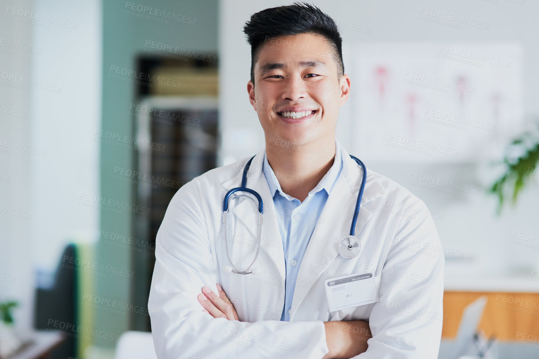 Buy stock photo Cropped portrait of a young male doctor standing with his arms folded in a hospital