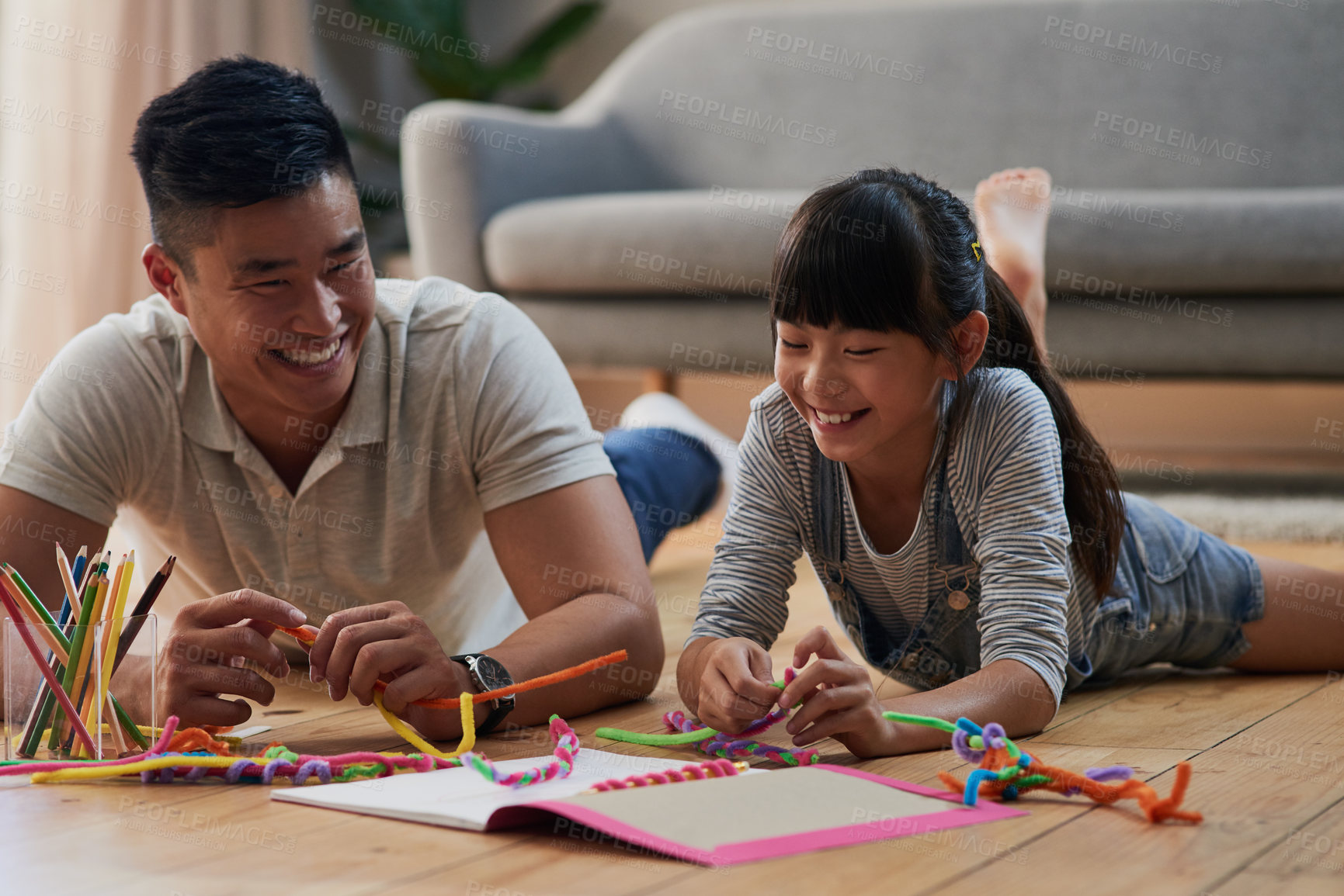 Buy stock photo Shot of a cheerful father and daughter doing homework together while lying on the floor at home during the day