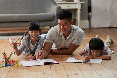Buy stock photo Shot of a cheerful father and his two children doing homework together while lying on the floor at home during the day