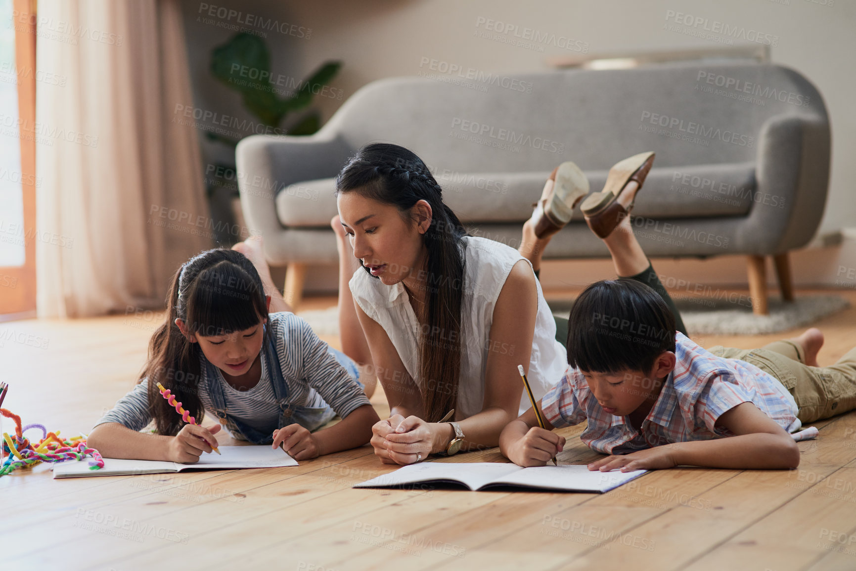 Buy stock photo Shot of a cheerful mother and her two children doing homework together while lying on the floor at home during the day